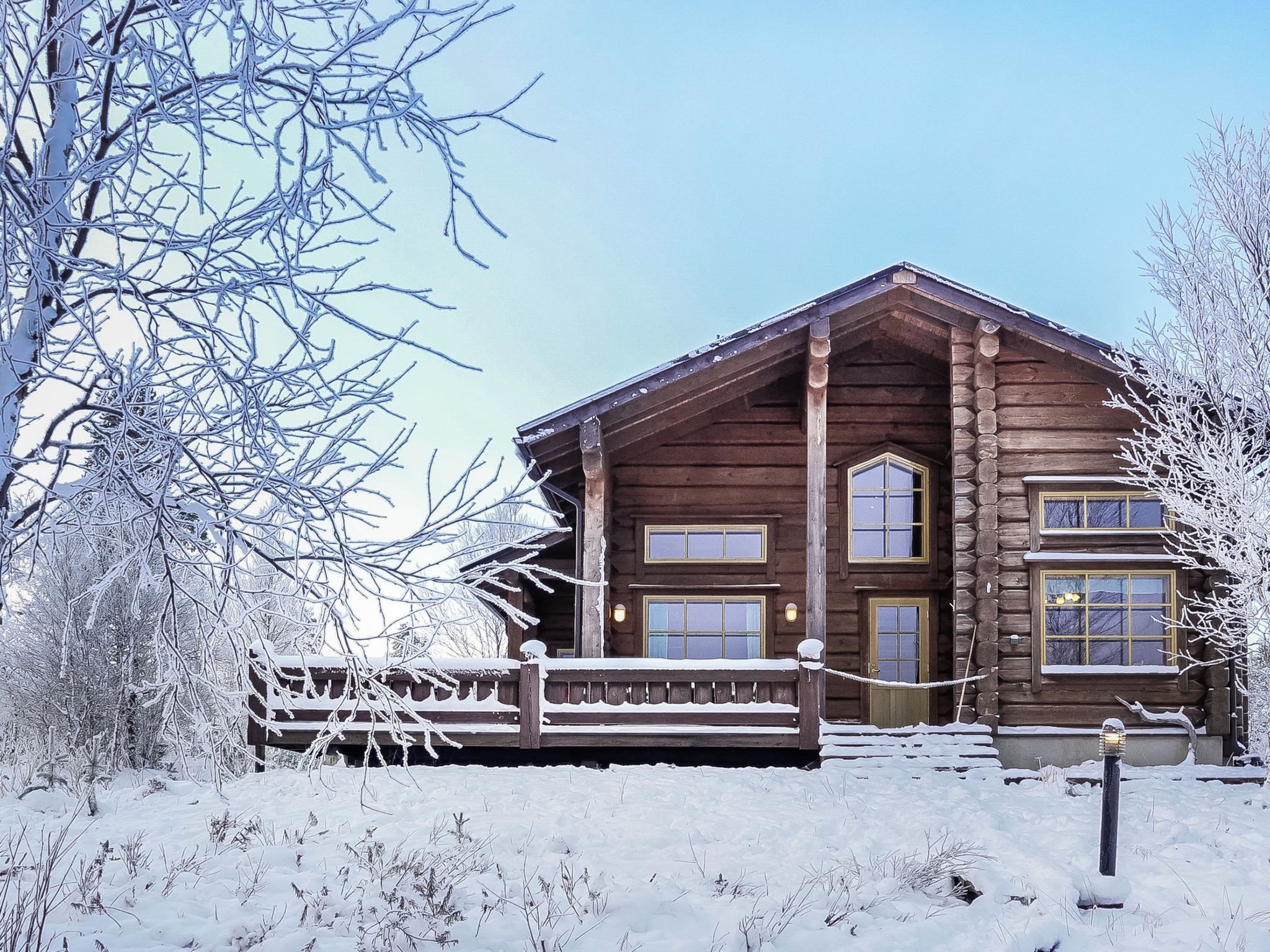 A wooden cabin with a porch, surrounded by snow-covered trees.
