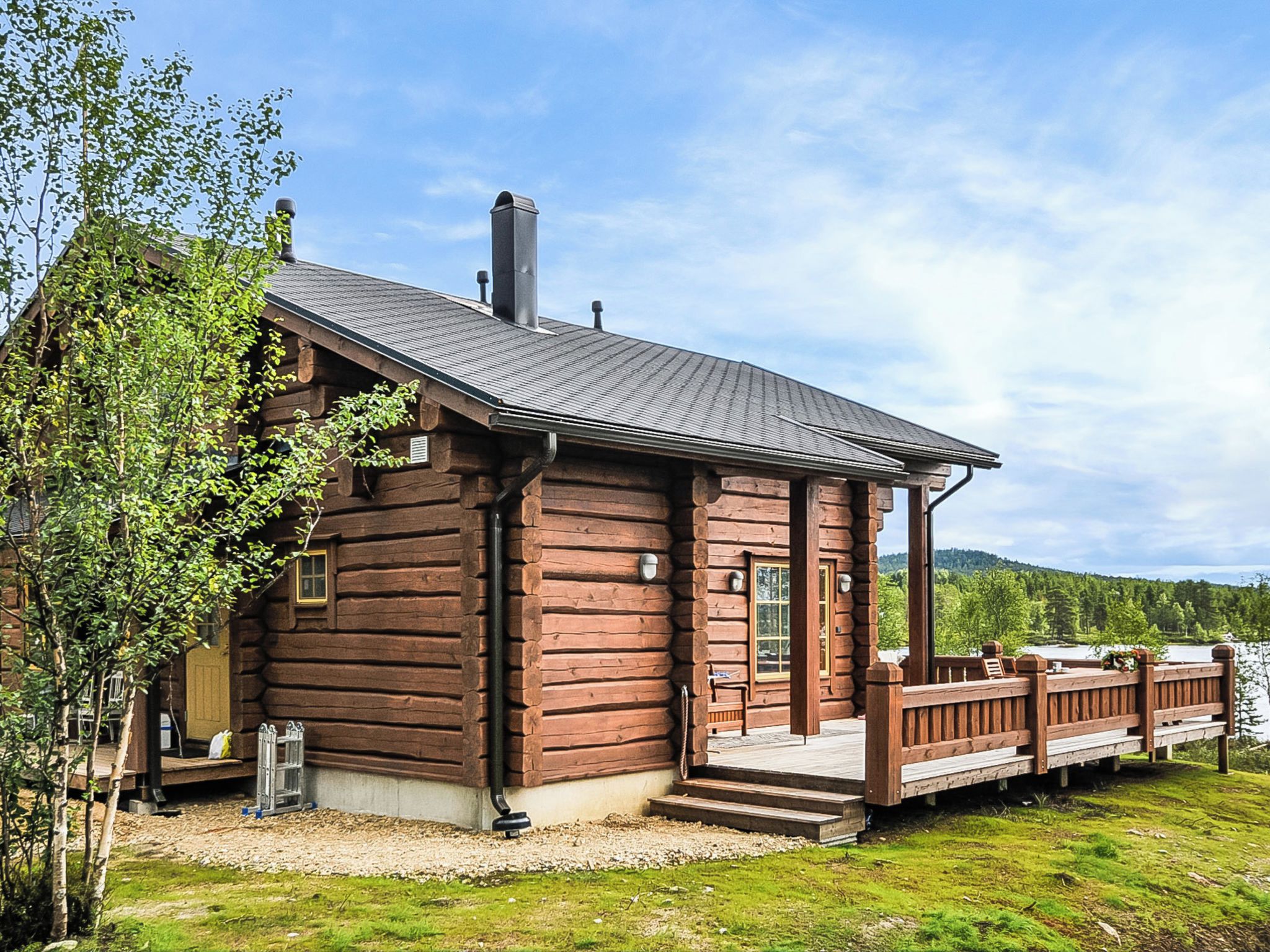 A log cabin with a deck overlooking a lake.