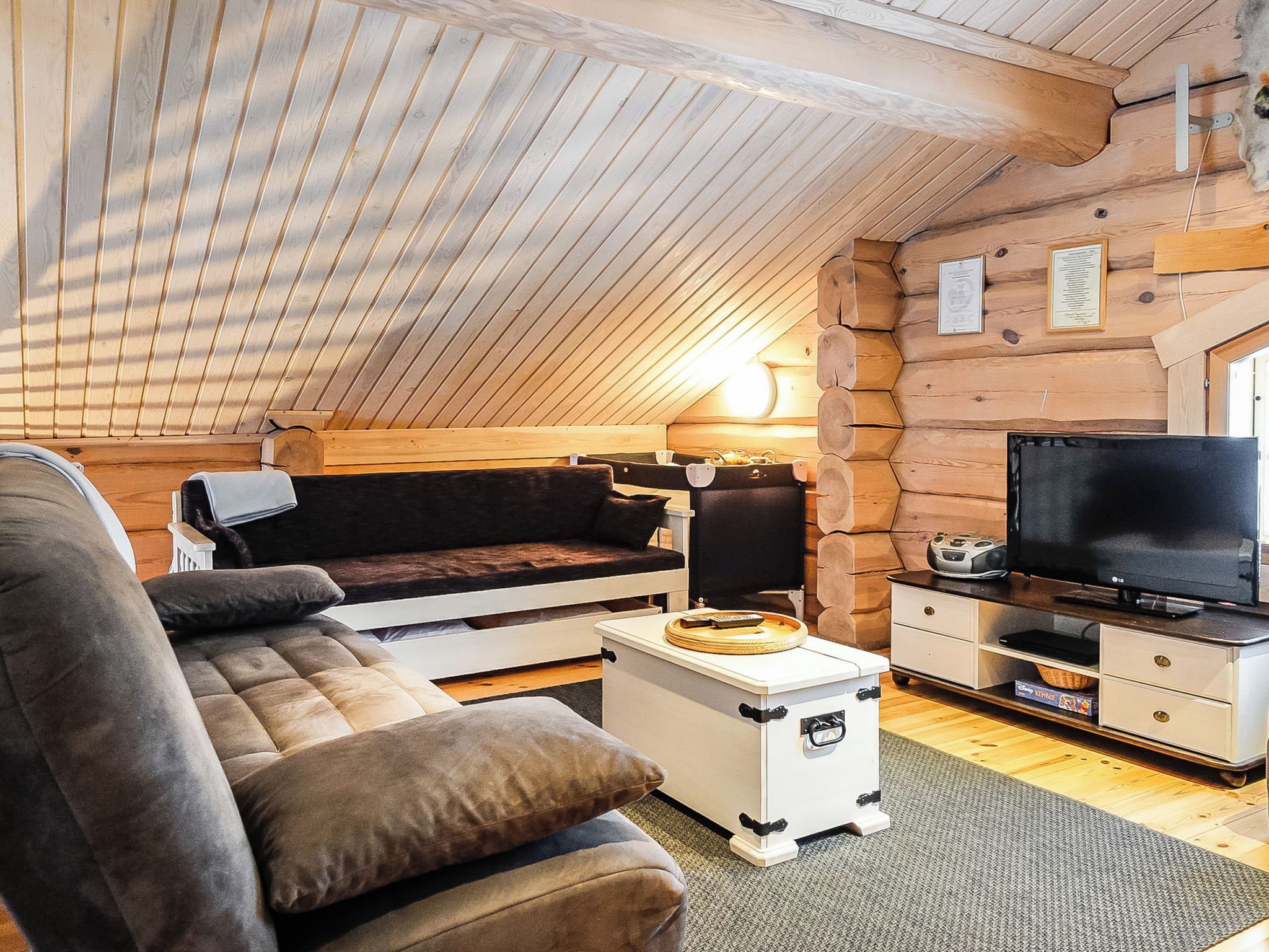 A cozy cabin interior with a sofa, a small table, a television, and a wooden ceiling.
