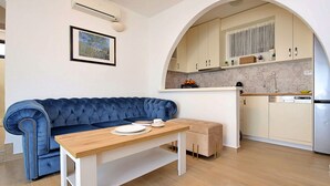 A compact living space with a blue sofa, a wooden table, and a kitchen area with a sink and cabinets. - Antoine by Interhome (Marina)