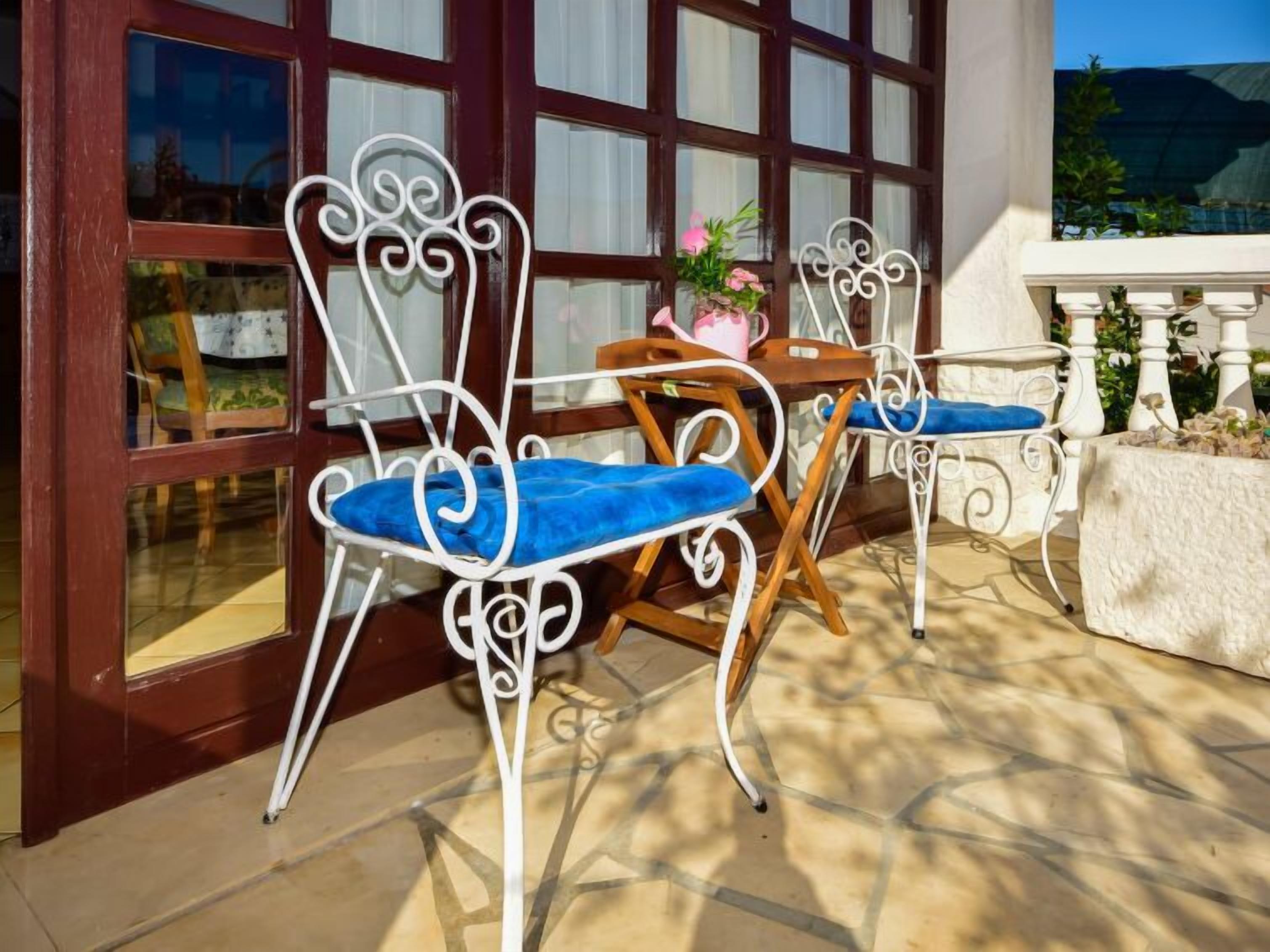 Zwei Terrassenstühle mit blauen Kissen, ein Holztisch und ein Blumentopf.