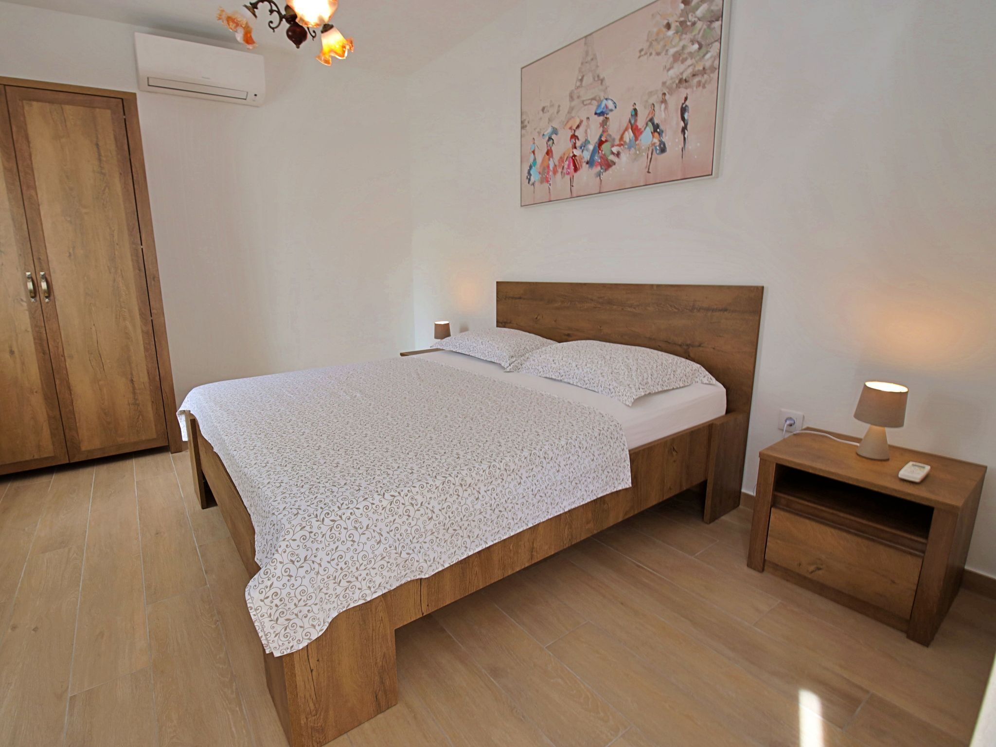 Ein Schlafzimmer mit einem Holzbett, einem Nachttisch mit Lampe, einem Kleiderschrank und einem Bild an der Wand.