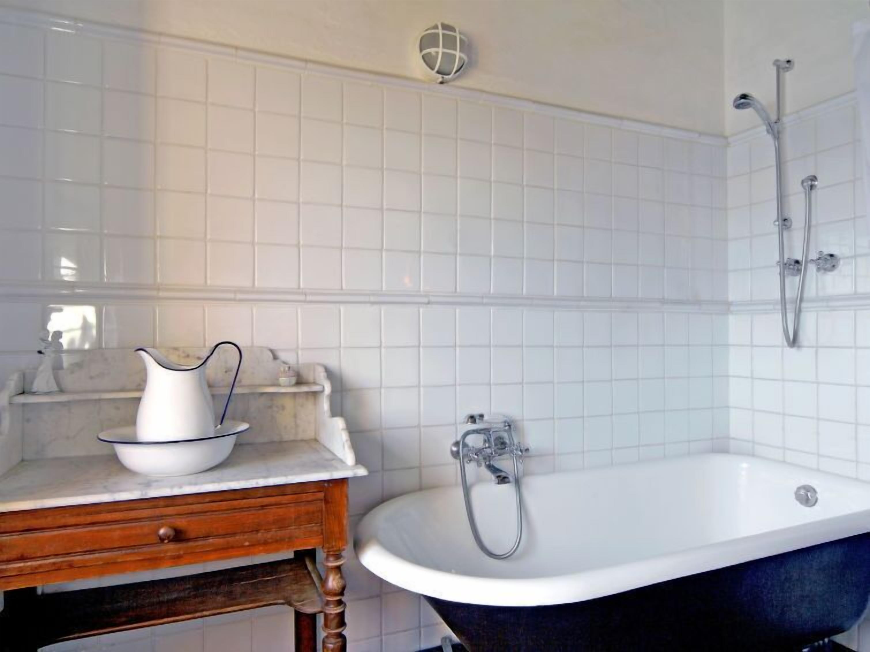 Une salle de bain avec une baignoire blanche, un meuble-lavabo en bois surmonté d’un plan de travail en marbre et un mur recouvert de carreaux blancs.