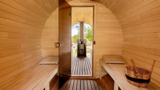 A sauna with wooden walls and benches, a sauna heater, and a wooden bucket. - Osada Ulnowo by Interhome (Grunwald)