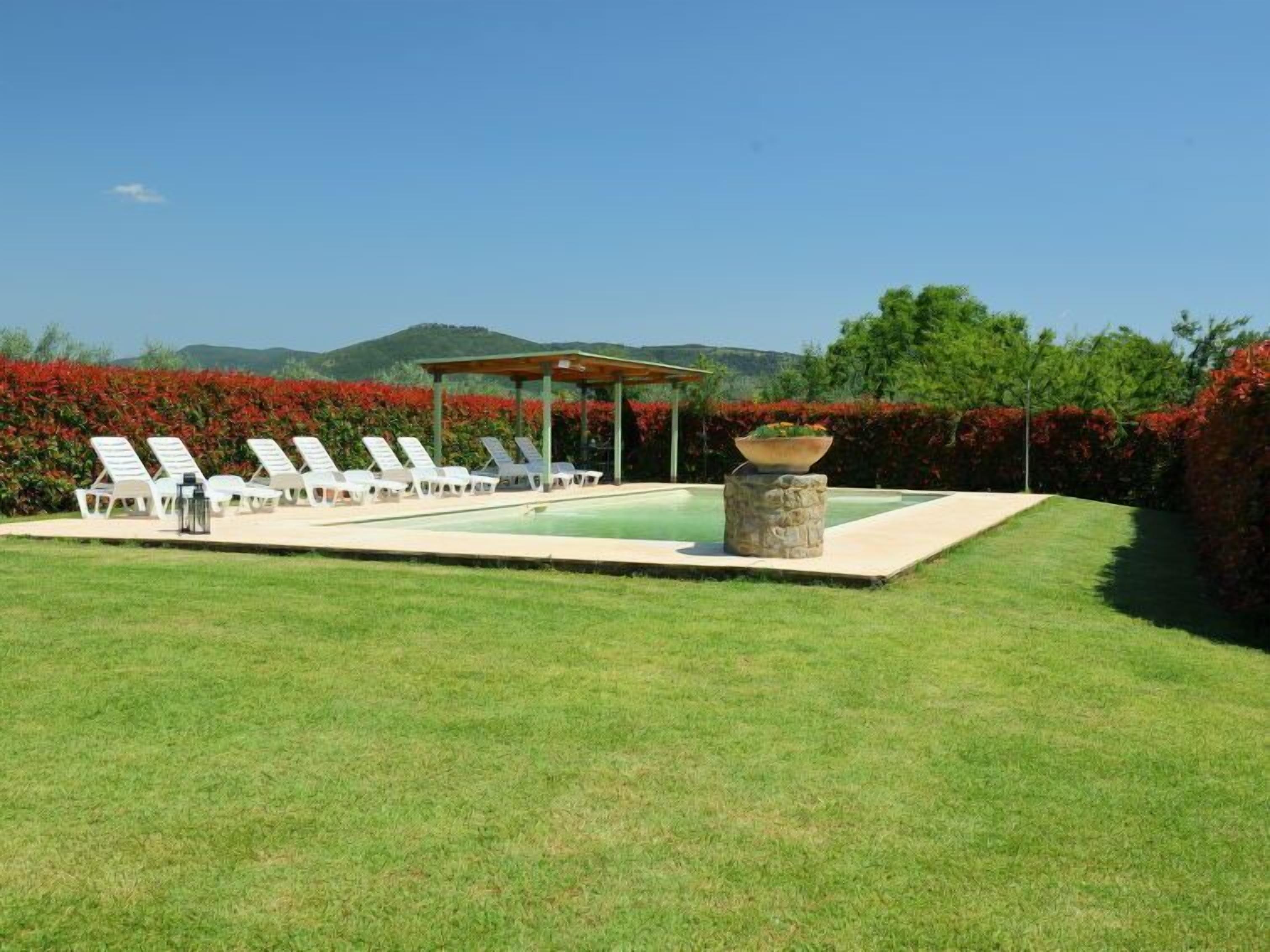 Zona de piscina con sillas de descanso, un espacio de estar cubierto y un elemento decorativo de piedra.