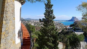 A stone building with a red staircase leading to a balcony overlooking a coastal cityscape with a mountain in the distance. - Vista Ifach by Interhome (Calpe/Calp)
