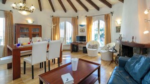 A spacious living room with a wooden dining table, white chairs, a blue sofa, and a fireplace. - Vista Ifach by Interhome (Calpe/Calp)