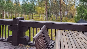 A wooden deck with a bench and a table, surrounded by a forest with tall trees.