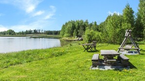 A lakeside picnic area with a wooden swing set, a table, and benches. - Niementalo 2 by Interhome (Kinnula)