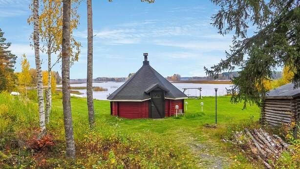 A small red cabin with a steep roof, surrounded by a grassy area and trees. - Niementalo 2 by Interhome (Kinnula)