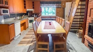 A kitchen with wooden cabinets, a dining table with chairs, a stove, and a window with a view of greenery. - Niementalo 2 by Interhome (Kinnula)