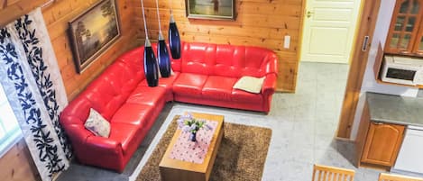 Un salon chaleureux avec un canapé d’angle rouge, un plafond en bois et un tableau accroché au mur.