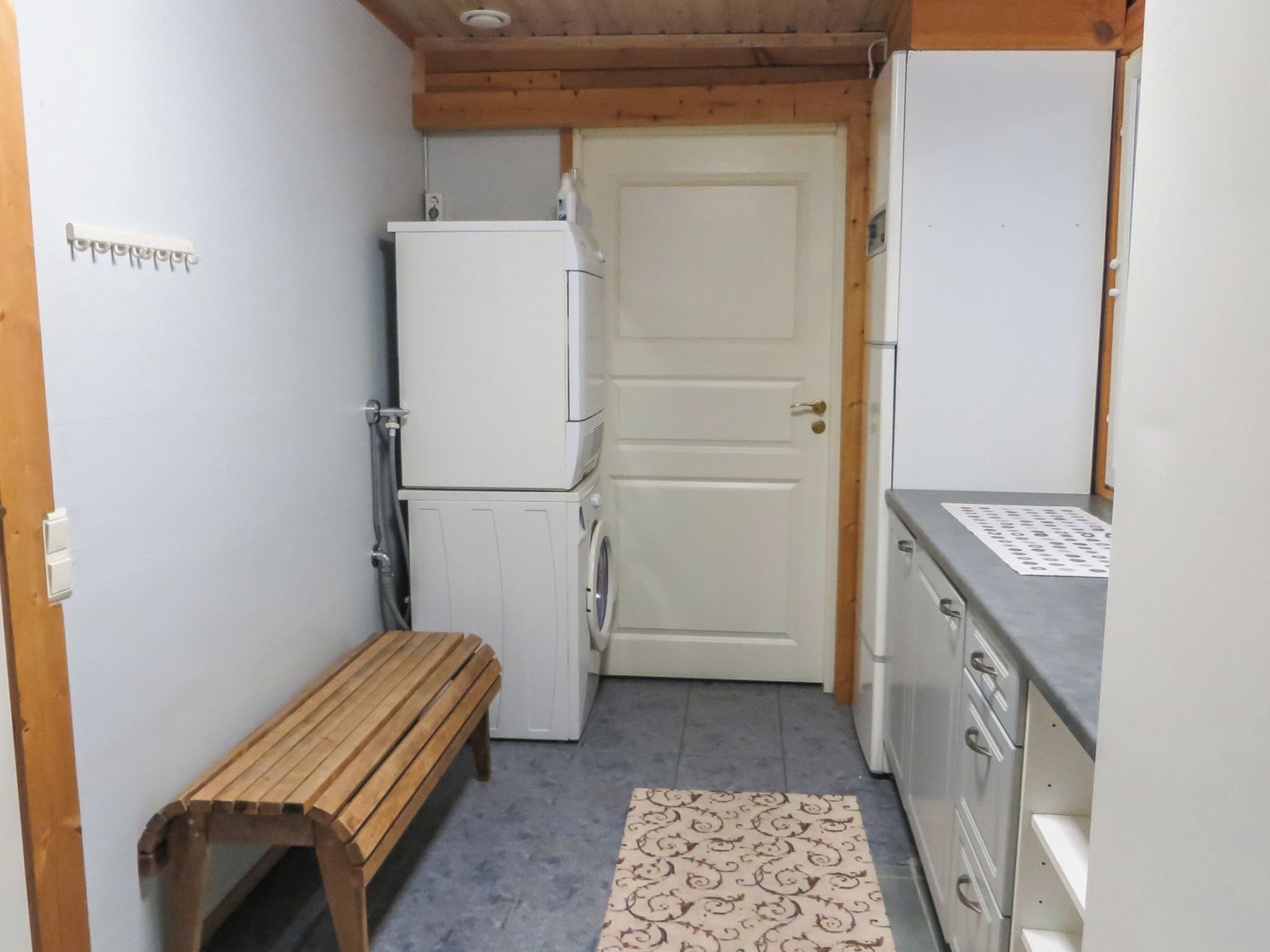 Una cocina compacta con refrigerador, lavadora y una banca.