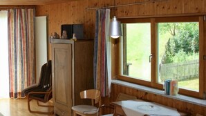 Un interior de madera con una mesa de comedor, dos sillas, un armario y un ventanal con vistas a la vegetación.