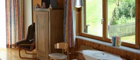 A wooden interior with a dining table, two chairs, a cabinet, and a window with a view of greenery.