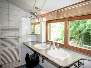 Ett modernt badrum med två handfat, en handdukshängare och ett fönster med utsikt över grönområden.