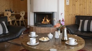 Un saló tranquil amb una llar de foc, dos sofàs de cuir, una taula de centre amb tasses i pastissos, i panells de fusta a les parets.