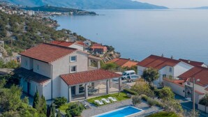 Eine Küstenwohngegend mit Häusern, die rote Ziegeldächer, einen Pool und Meer- und Gebirgsblick haben.