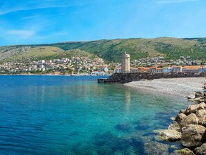 Une ville côtière dotée d’un phare imposant, d’eaux d’un bleu limpide et d’une colline densément bâtie, parsemée de bâtiments aux couleurs vives.