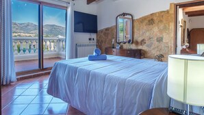 Un dormitorio con una cama grande, un aparador, un espejo, un televisor y un balcón con vistas a montañas.