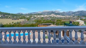 Un balcón con vista a una piscina, una cordillera y un pueblo al fondo.
