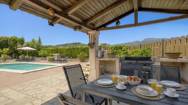 Un patio al aire libre con una mesa lista para el desayuno, una parrilla y una piscina al fondo.