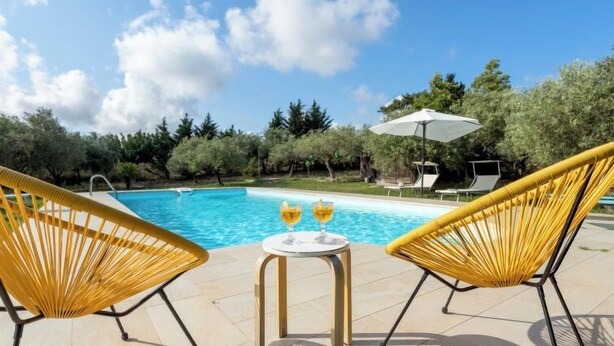 Zona de piscina con dos sillas amarillas y una mesa con dos copas de vino.