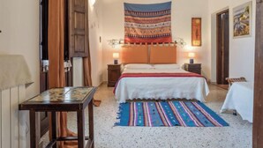 Un dormitorio con una cama, dos mesitas de noche con lámparas, un tapiz y una alfombra estampada.