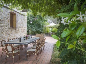 Un espace de restauration en plein air avec un mur en pierre, une longue table entourée de chaises et un jardin en arrière-plan.