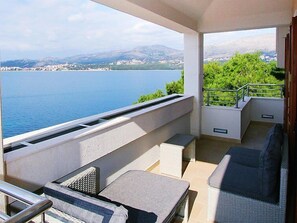 A balcony with a view of a lake and mountains, furnished with wicker chairs and a small table.