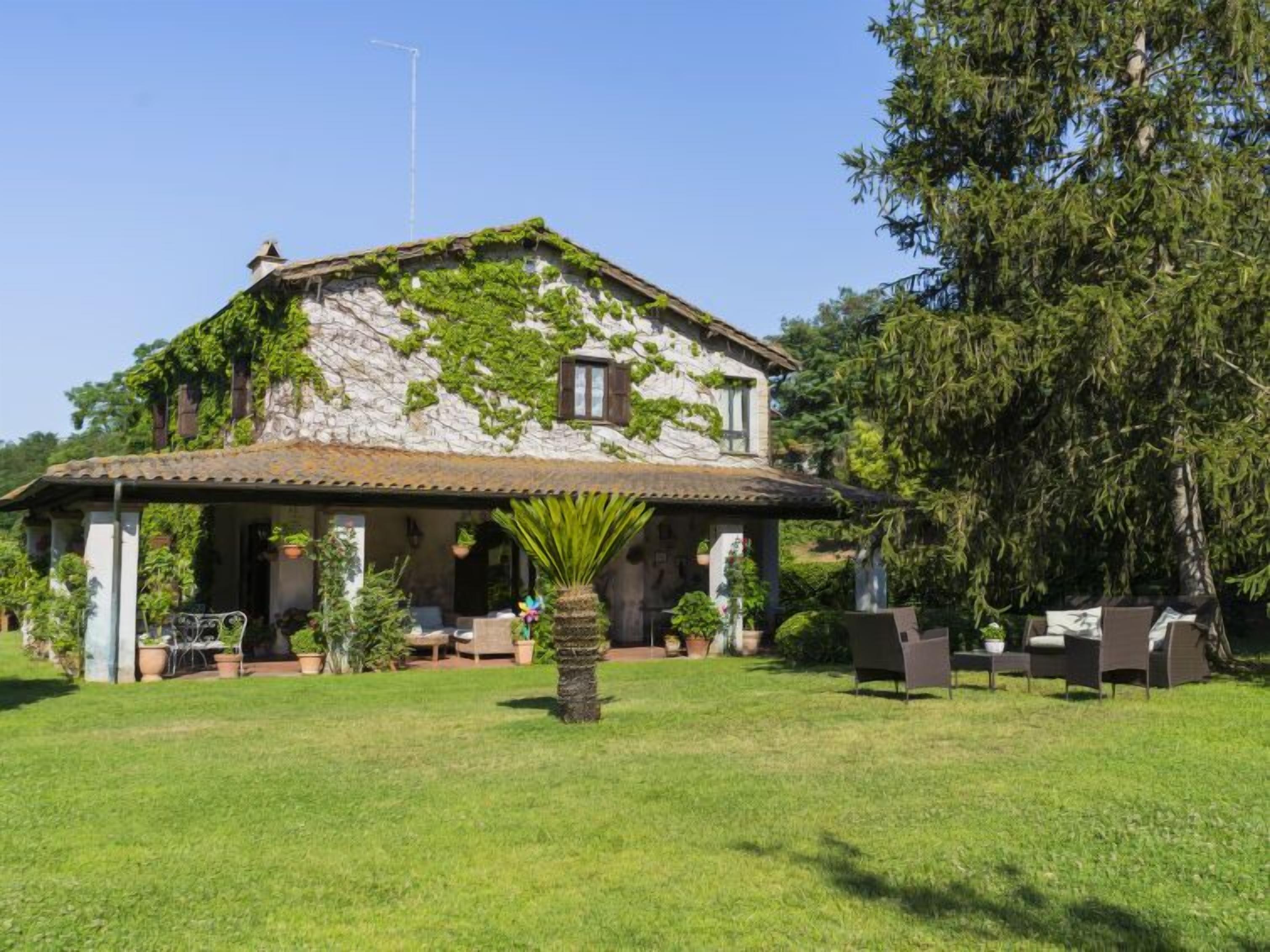 A stone house with a tiled roof, ivy-covered walls, and a covered patio with outdoor furniture.