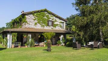 A stone house with a tiled roof, ivy-covered walls, and a covered patio with outdoor furniture.