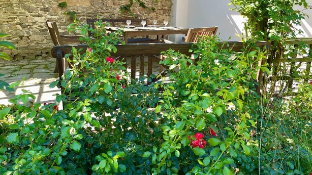 A stone wall with climbing plants, a wooden table with chairs, and a pergola structure.