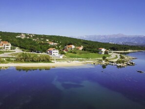 Un village au bord d’un lac, avec des maisons qui bordent la rive et une chaîne de montagnes en arrière-plan.