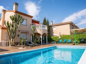 Una piscina con lettini, un'area salotto coperta e un edificio con tetto in tegole rosse e cactus.