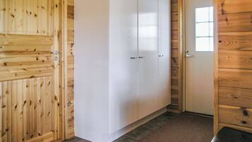 A wooden interior with a white wardrobe, a door with a window, and a brown mat on the floor.