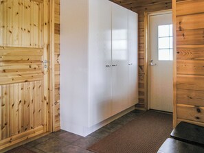 Un interior de madera con un armario blanco, una puerta con ventana y un felpudo marrón en el suelo.