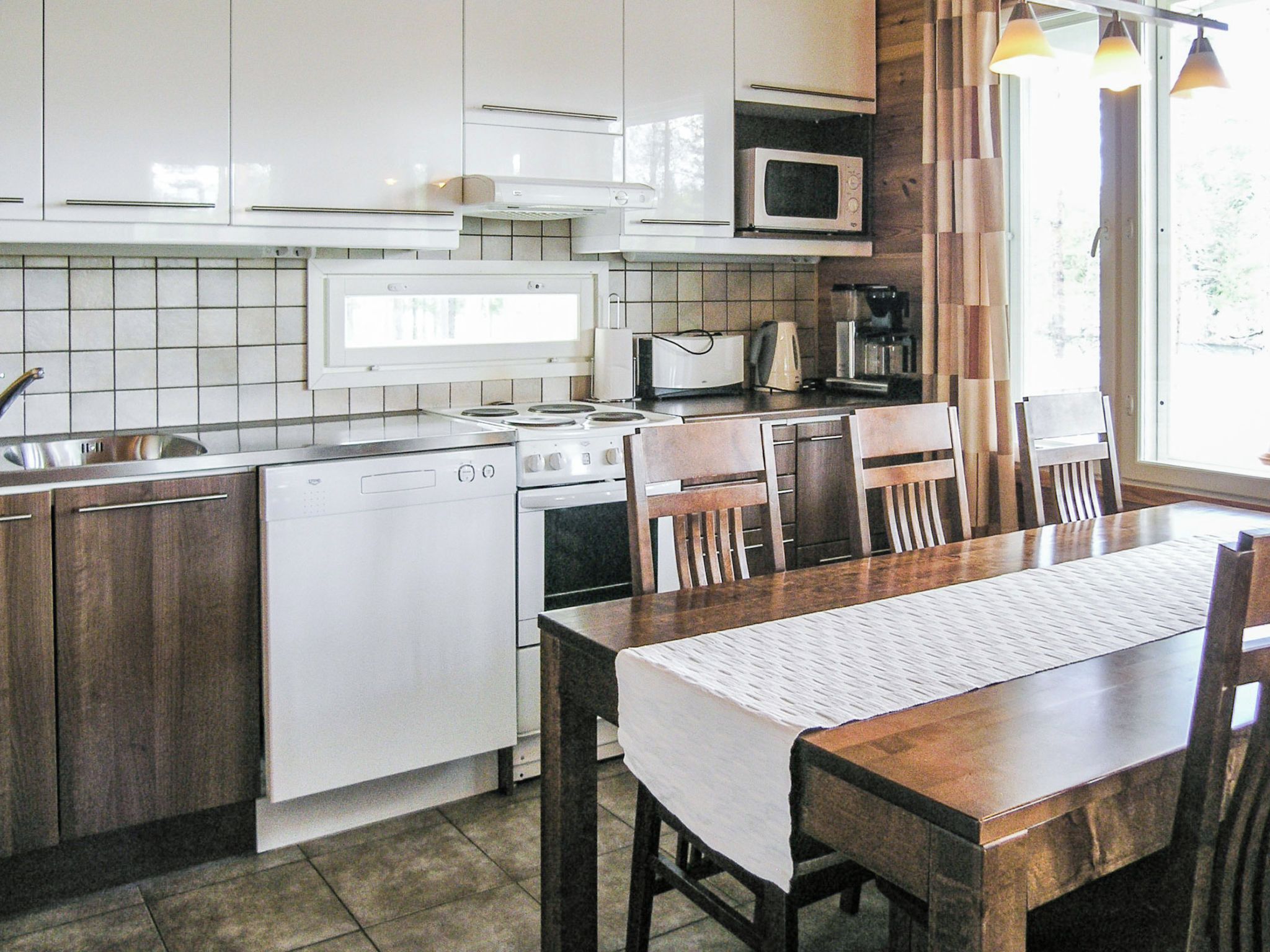 A kitchen with white appliances, a dining table with chairs, and a window with curtains.