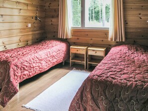Une chambre avec deux lits simples, une fenêtre avec des rideaux et une petite table de chevet en bois placée entre les lits.