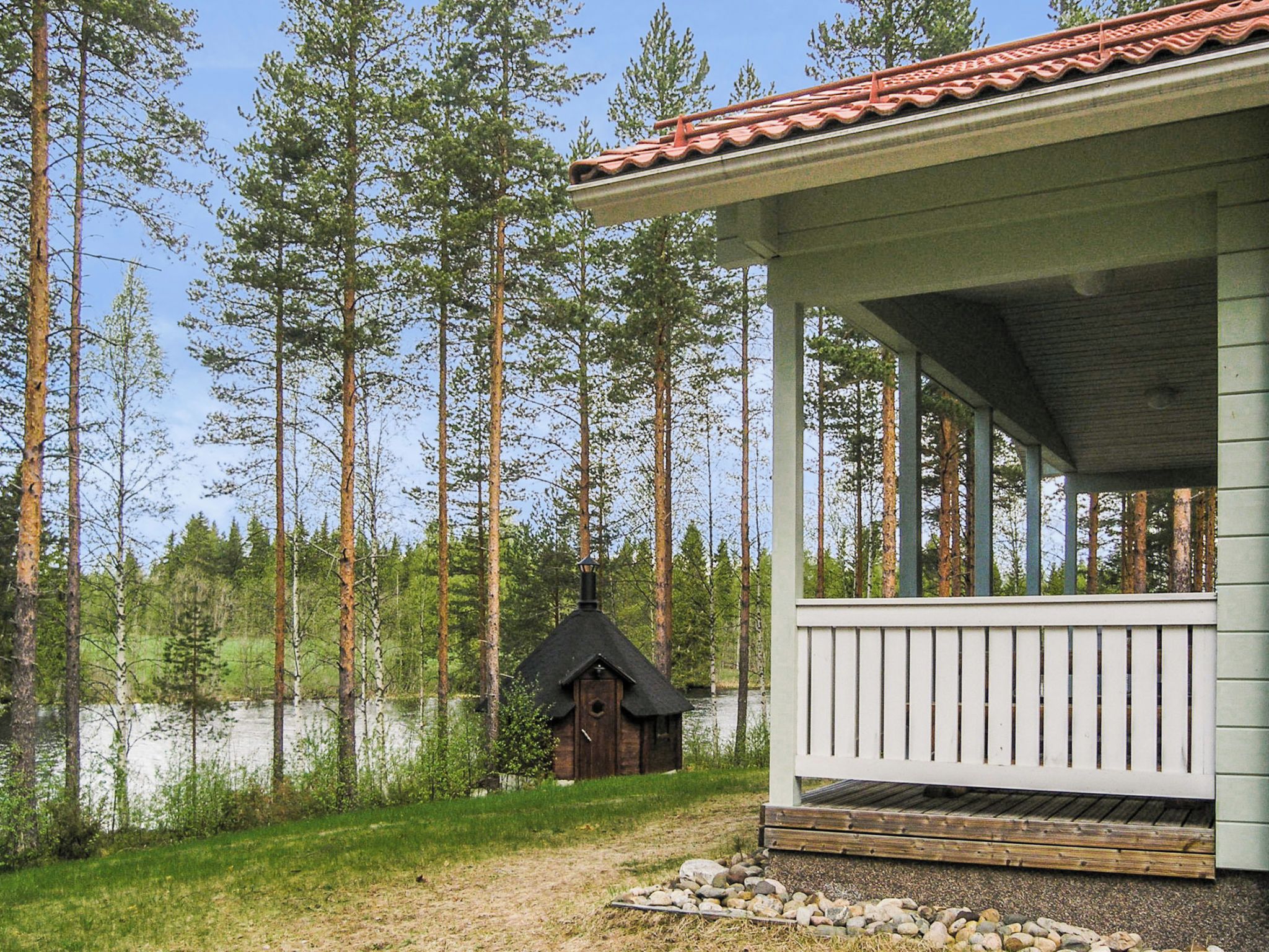 A cabin with a porch, surrounded by a forest and a lake.