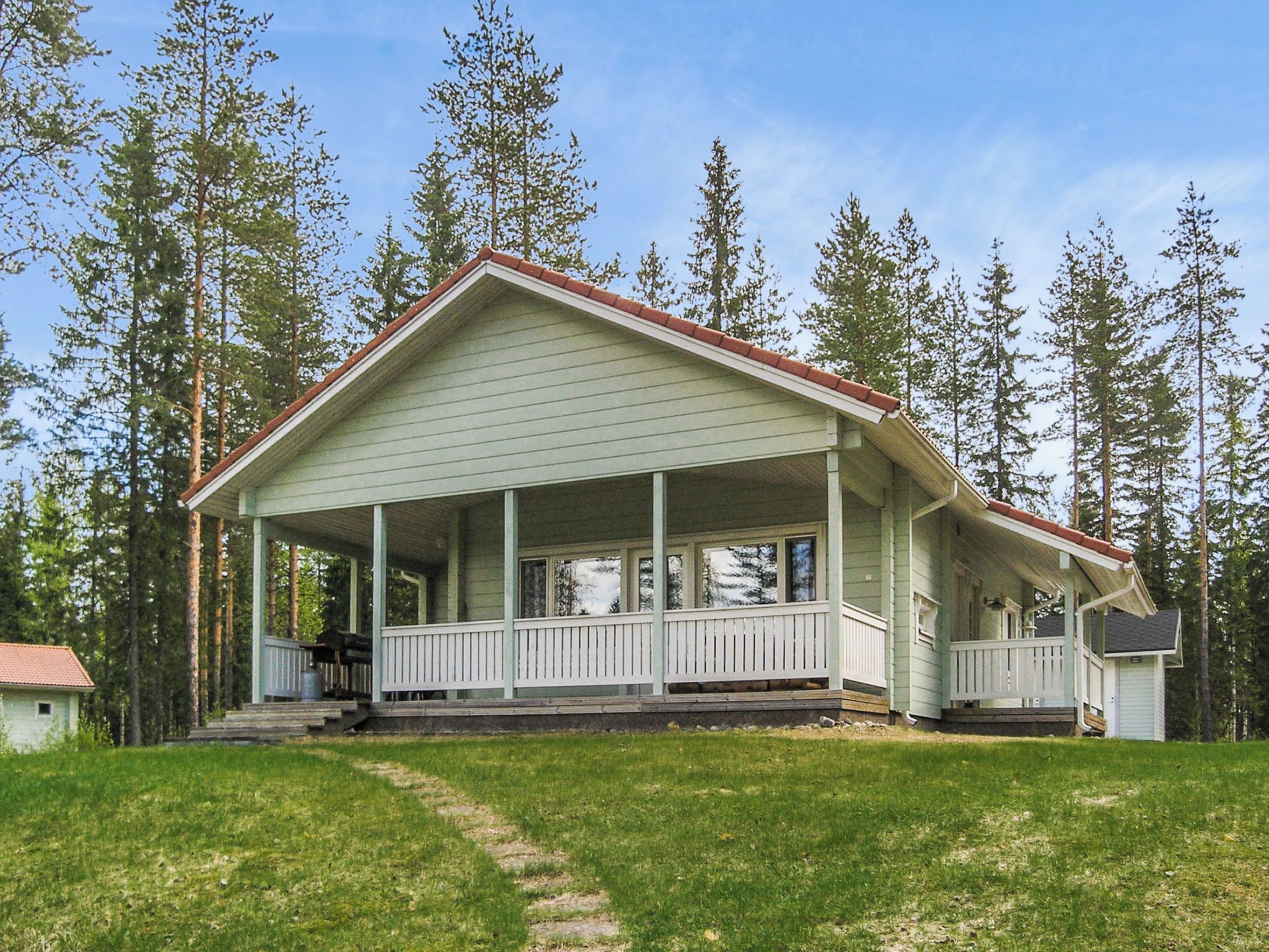 A two-story house with a porch, surrounded by tall trees.