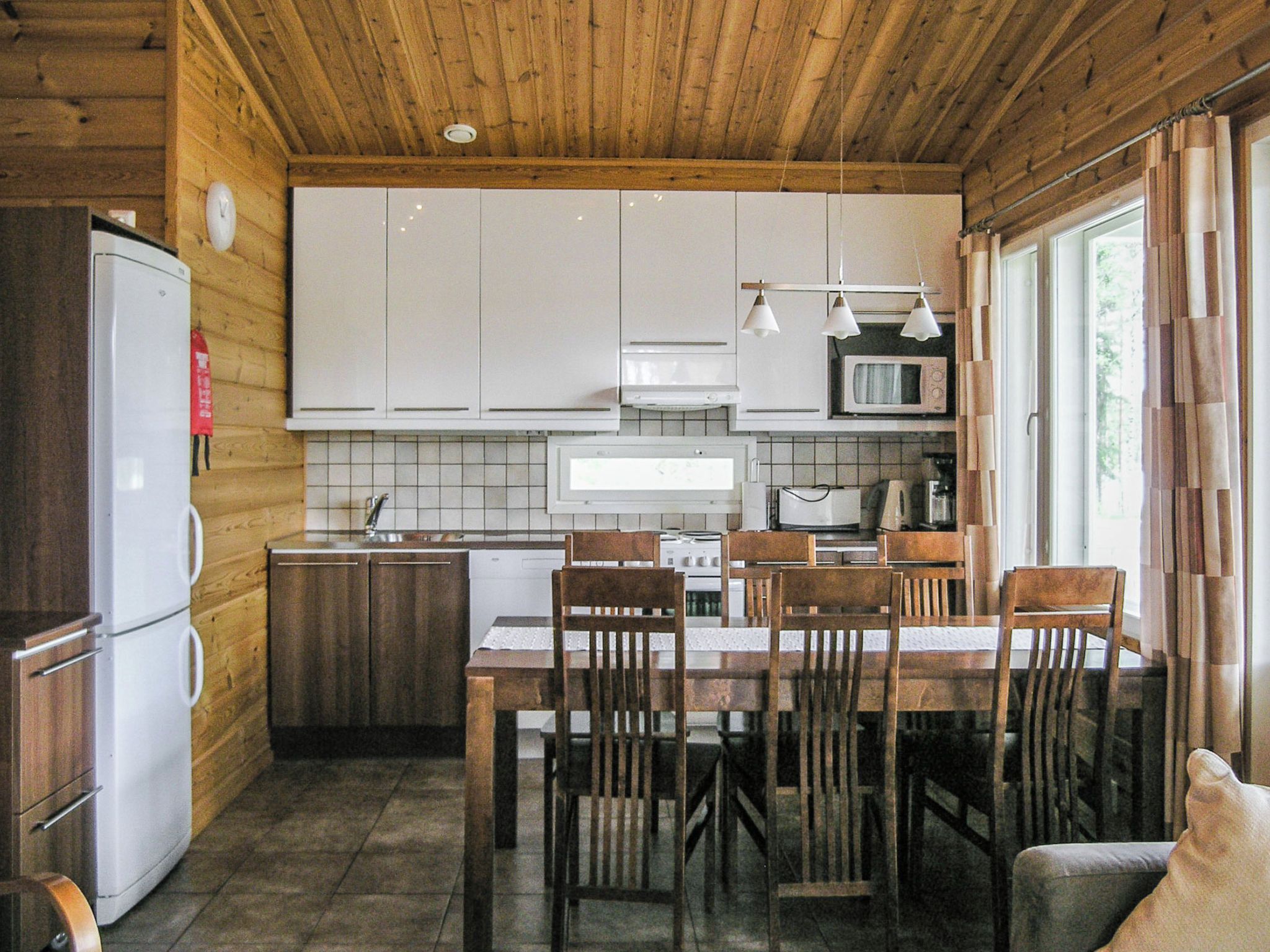 Una cocina funcional con armarios de madera, una mesa de comedor con sillas, un refrigerador y un microondas.