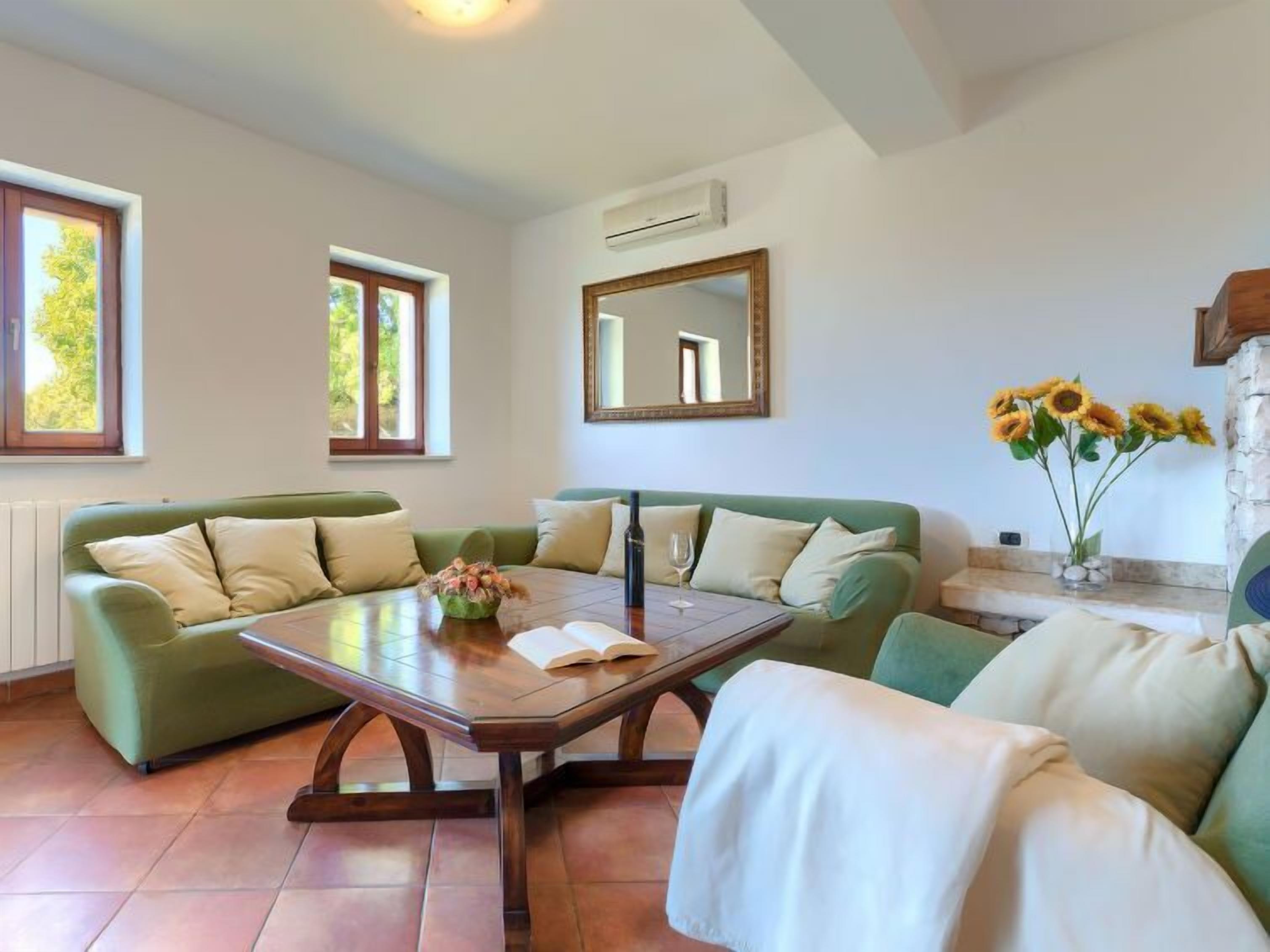 A living room with two green sofas, a wooden coffee table, and a vase with sunflowers.