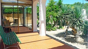 A patio area with a glass door leading to a room, surrounded by tropical plants and a brick floor. - Marinada by Interhome (L'Ampolla)