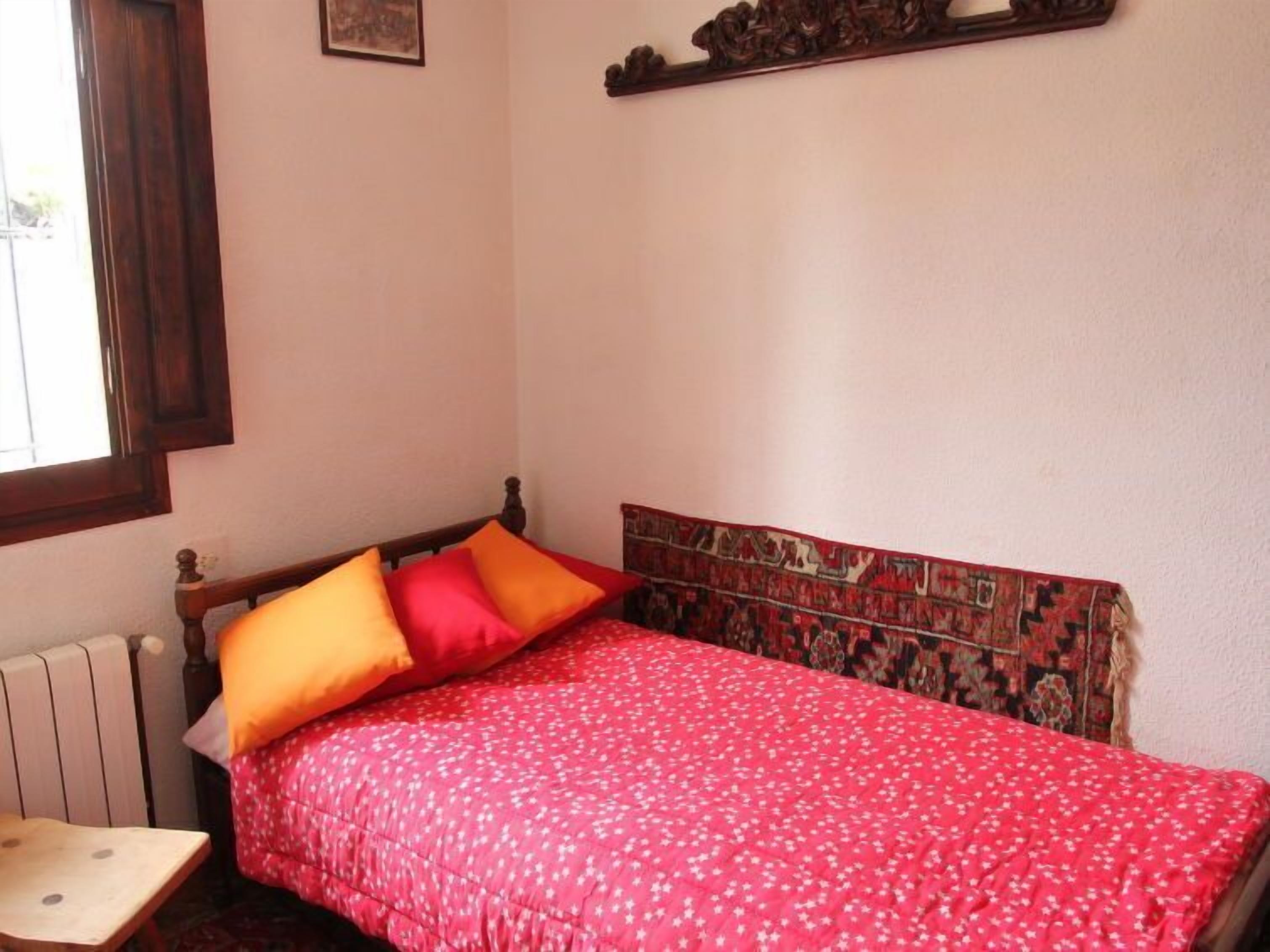 A small bedroom with a single bed, a wooden headboard, and a window.