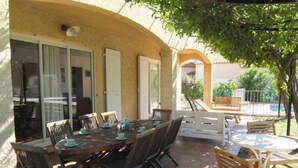 Une terrasse extérieure avec une table à manger pour six personnes, entourée de chaises en bois.