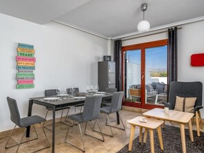 A modern dining area with a table set for four, chairs, a small side table, and a view through a glass door to the outside.