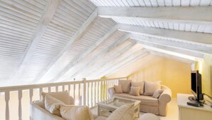 A cozy attic room with a sloped ceiling, a white railing, a beige sofa, a small table, and a television. - Les Vendanges by Interhome (Narbonne-Plage)