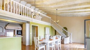 A spacious dining area with a wooden floor, white chairs, and a central table. A staircase with a white railing leads to an upper level. - Les Vendanges by Interhome (Narbonne-Plage)