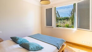 Ein Schlafzimmer mit Bett, Fenster mit Blick auf Grünflächen und einer Hängelampe.